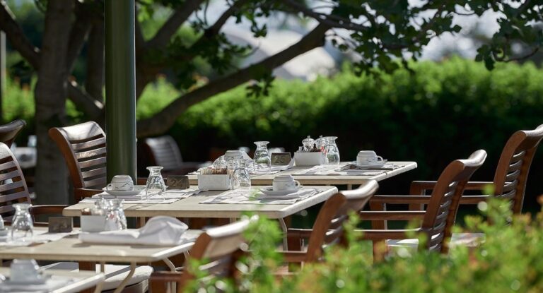 Tables set under the trees on a restaurant terrace, St Nicolas Bay Resort Hotel and Villas