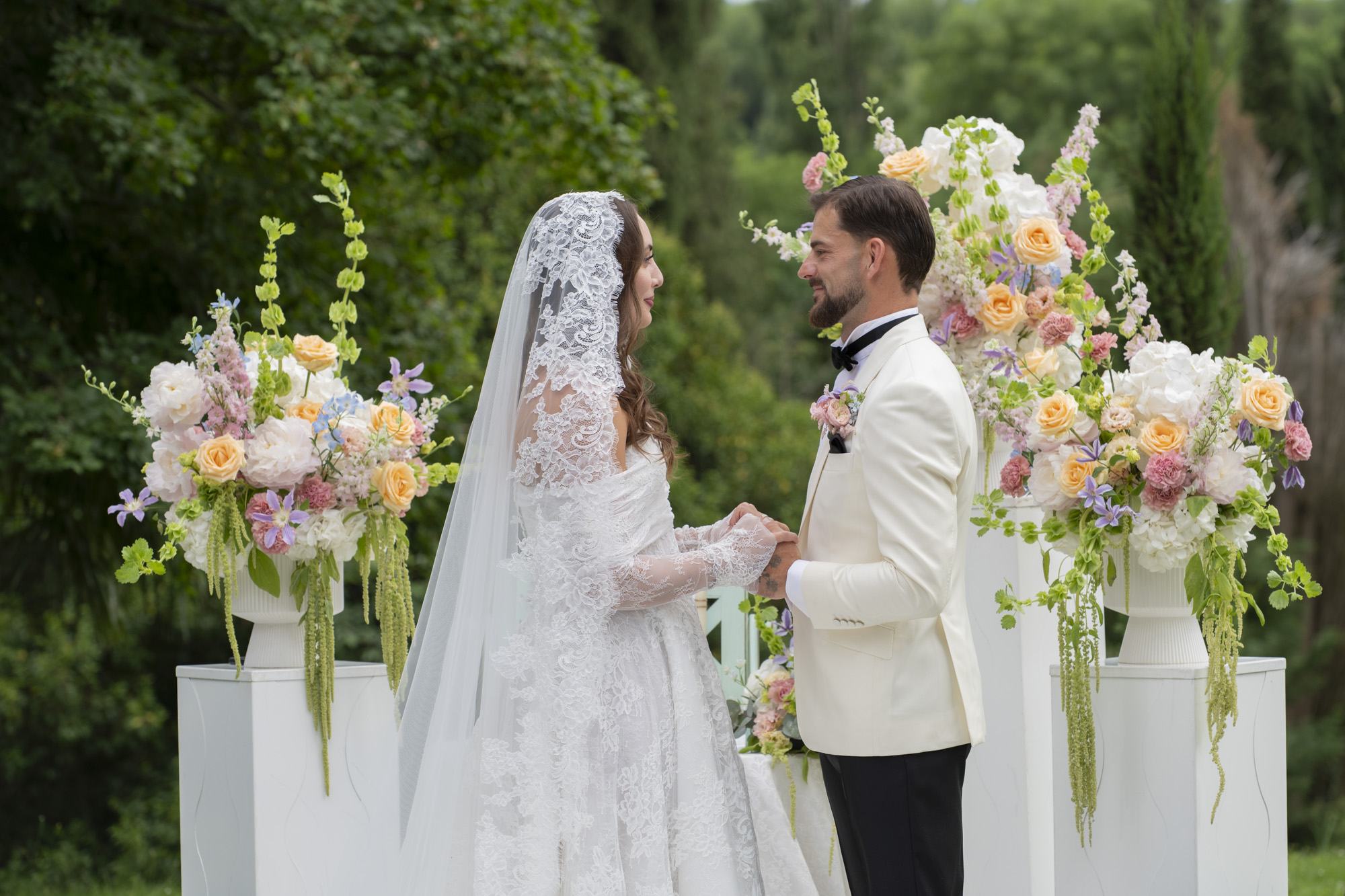 Vows exchanged between two tall arrangements of pastel flowers at an outdoor ceremony, Stefano Lunardi