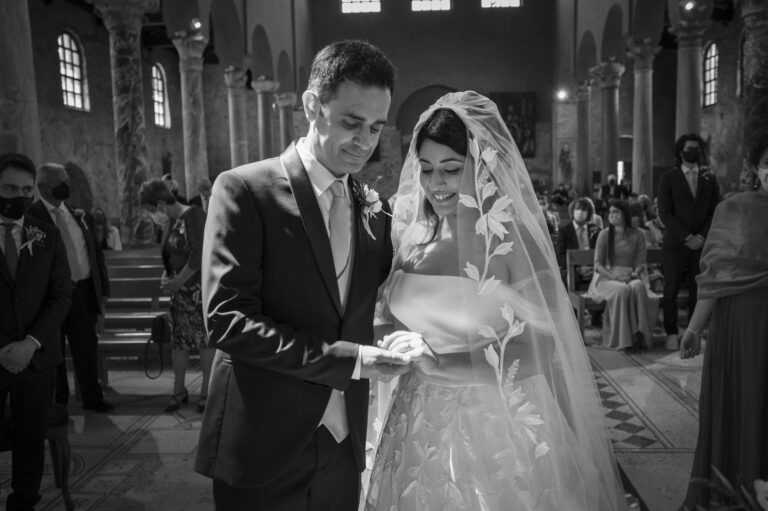 The groom placing the ring during a church ceremony, guests looking on, in black and white, Stefano Lunardi
