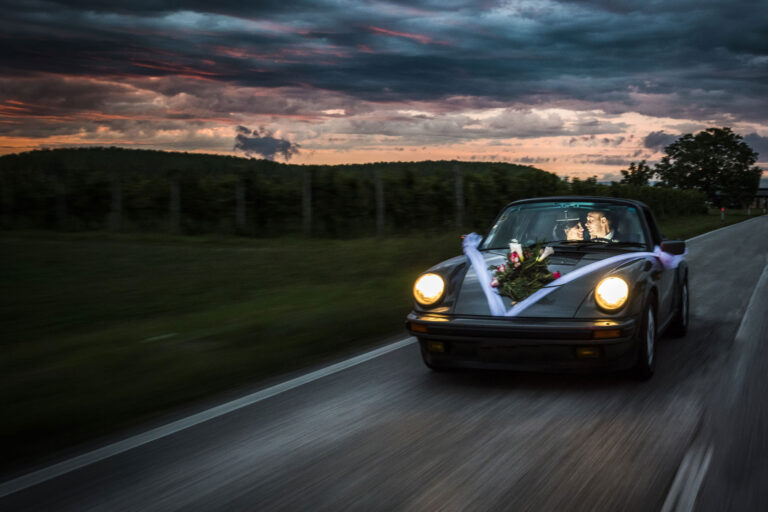 The couple leaving in a decorated Porsche along a country road at dusk, Stefano Lunardi