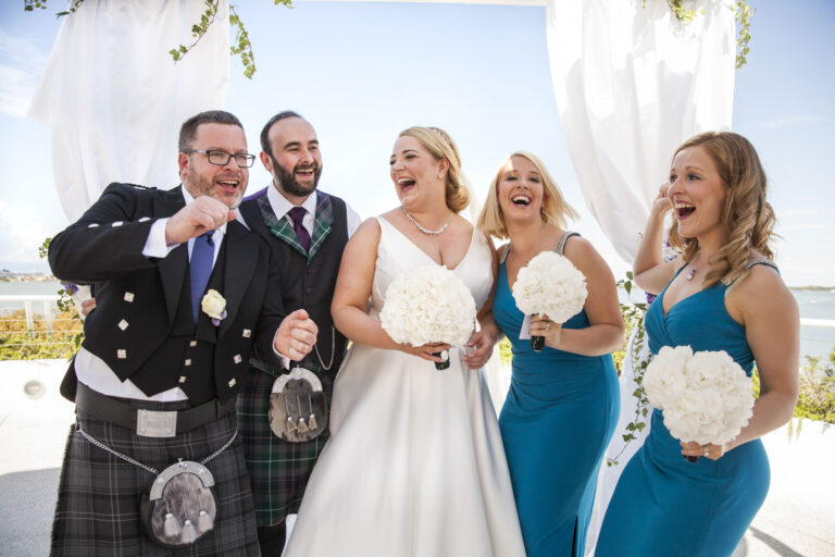 The bride laughing with the groomsmen in kilts and bridesmaids at a waterside wedding in Venice, Stefano Lunardi