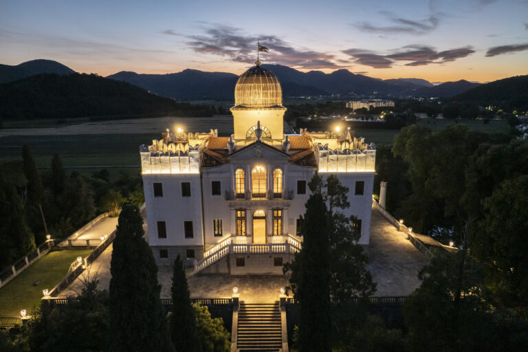 A domed villa lit up at dusk, seen from the air with the mountains beyond, Stefano Lunardi