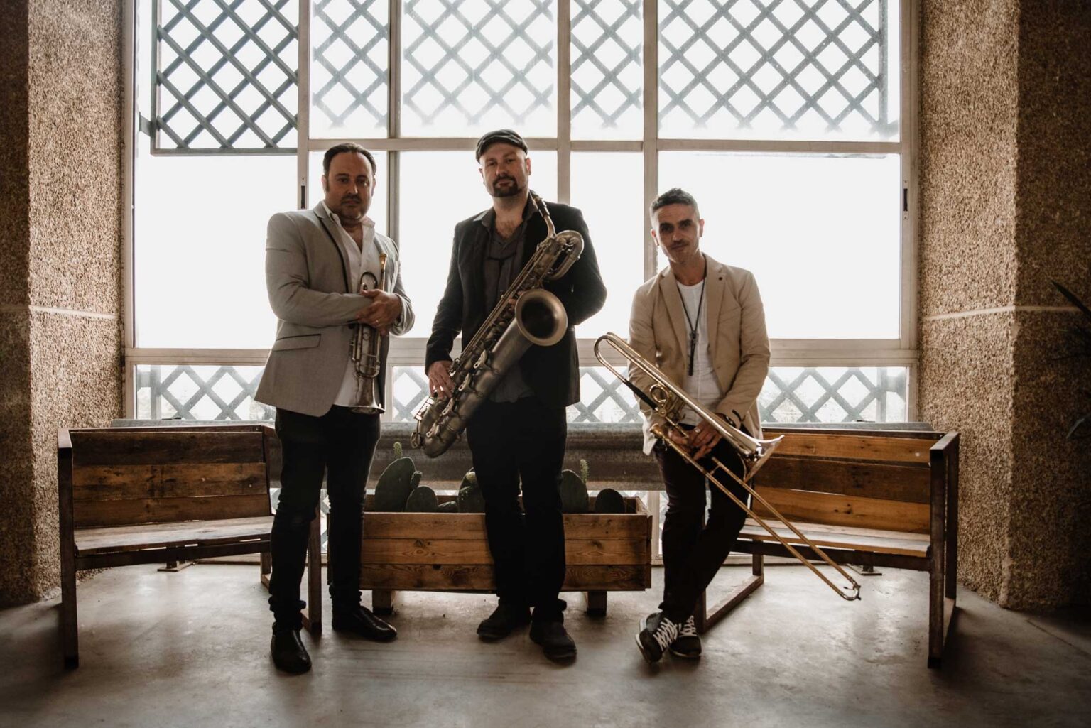 The brass section holding baritone saxophone and trombone in front of lattice windows
