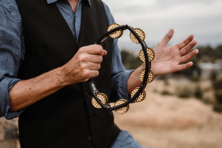 A musician in a waistcoat holding a tambourine outdoors, Stereo Star Band