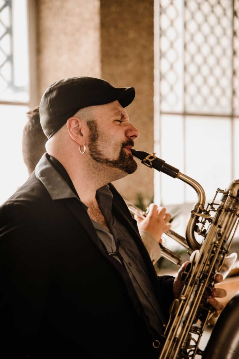 A saxophonist playing a baritone saxophone beside a window, Stereo Star Band