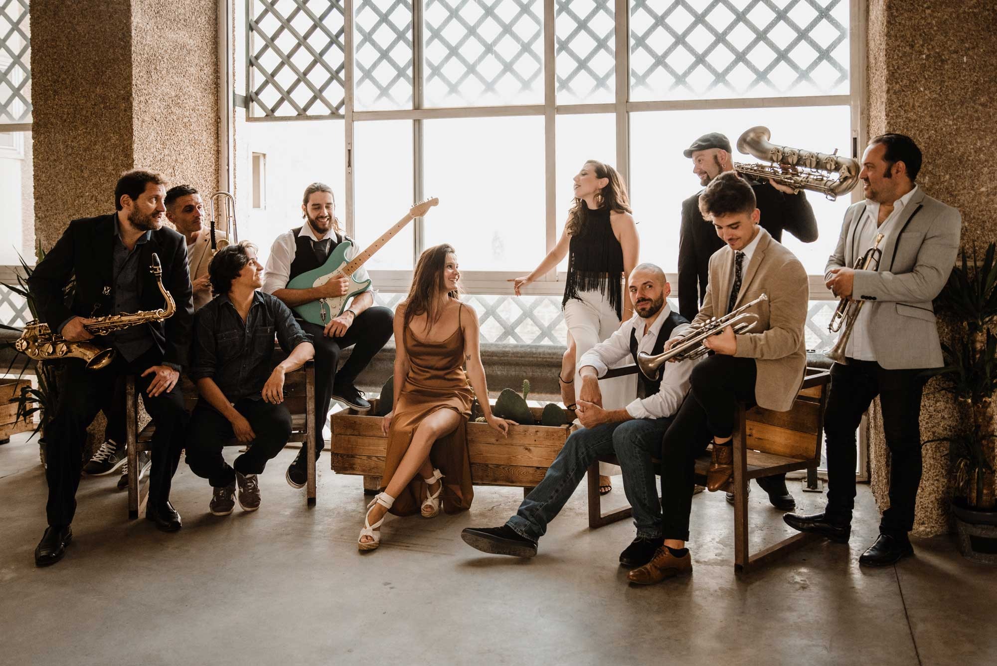 Band members seated and standing on wooden benches beside tall lattice windows with saxophones and a trumpet, Stereo Star Band