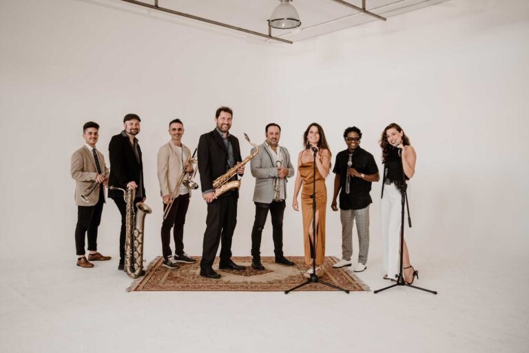 Singers, horns and rhythm section in a line against a white backdrop, Stereo Star Band