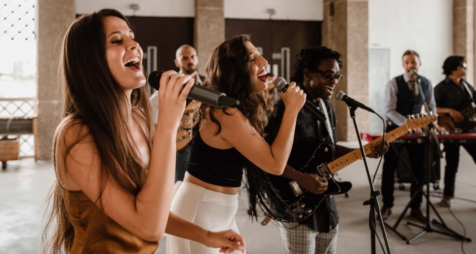 Two female vocalists singing together with the band behind them