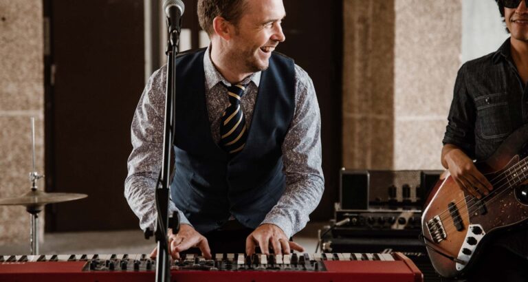 A keyboard player singing at the microphone with a bassist behind him, Stereo Star Band