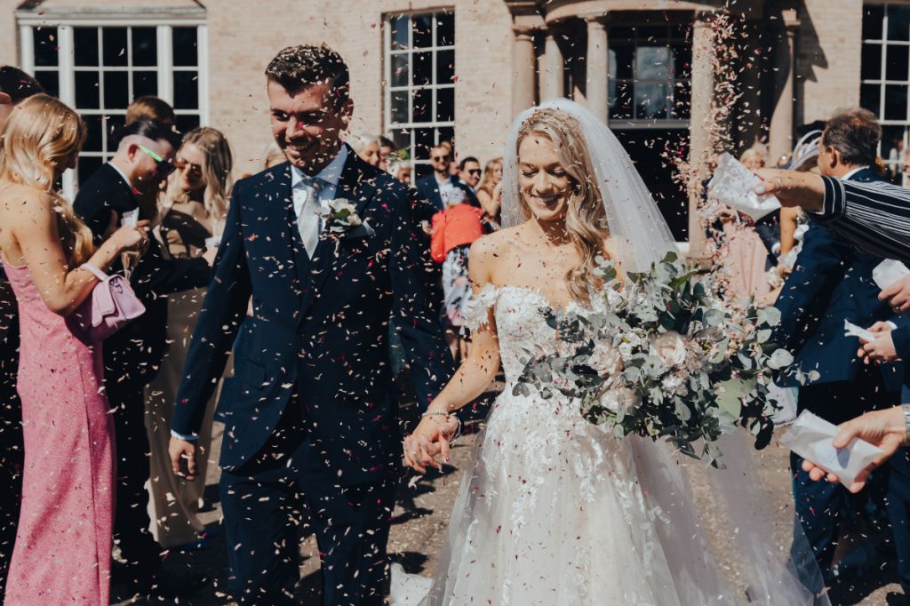 A couple walking through a shower of confetti outside the house
