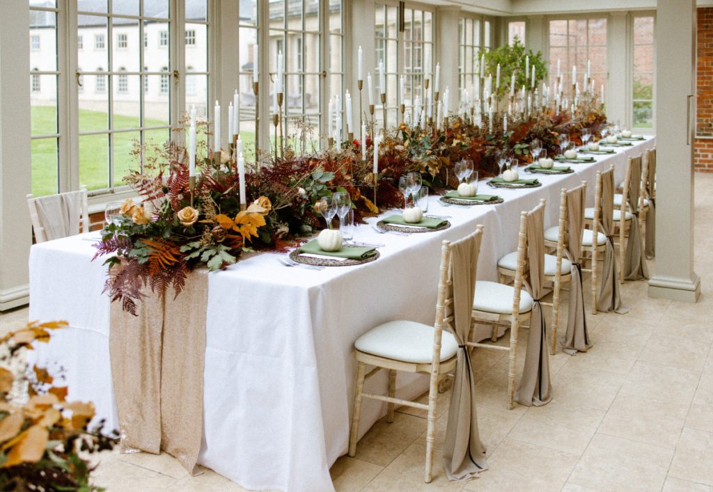 A long table dressed with autumn flowers in a glazed room