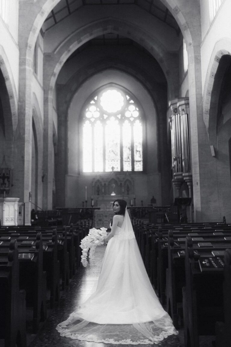 Black and white: a bride in the aisle of St James Church, Florence, light falling through the tall Gothic window behind her, Studio Fotografico Bacci
