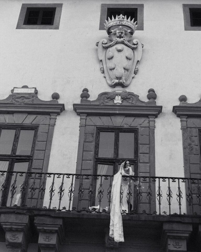 Black and white: the bride on a balcony beneath the stone coat of arms at Tenuta di Artimino, Studio Fotografico Bacci
