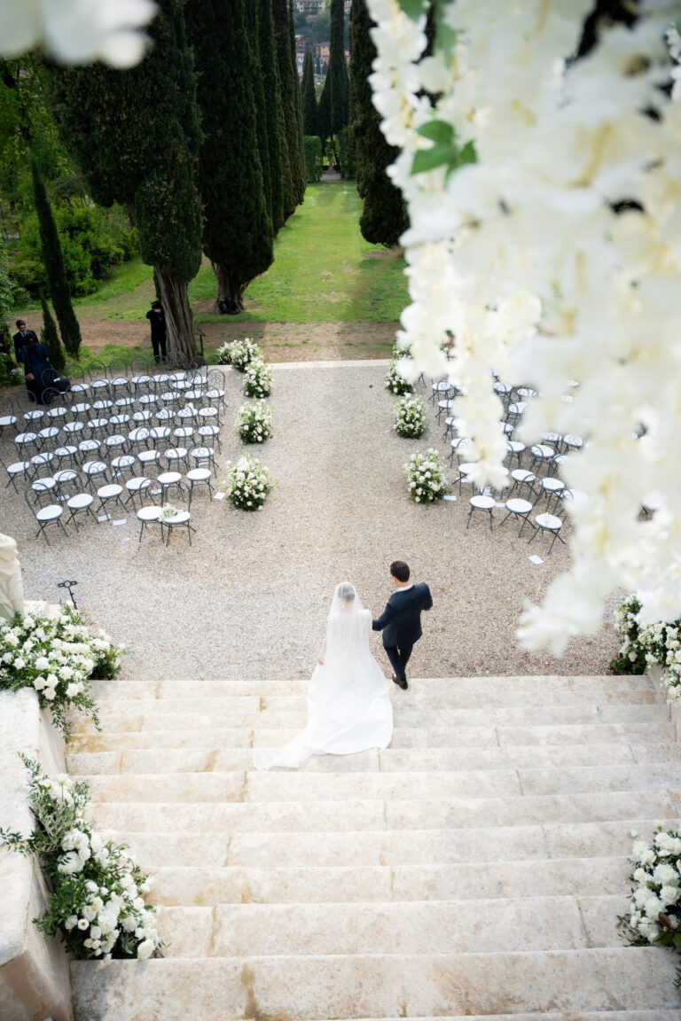 The couple walking down a stone staircase to the ceremony in a cypress garden in Verona, Suellen Fernandes Weddings & Celebrations