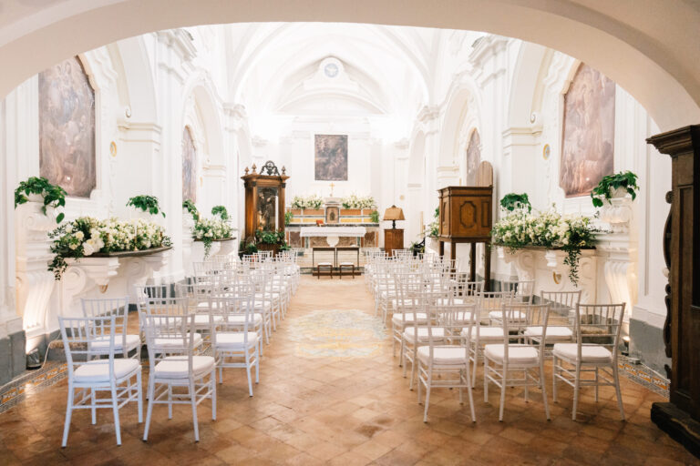A church interior on the Amalfi Coast laid for the ceremony, white chairs and white flowers along the aisle, Suellen Fernandes Weddings & Celebrations