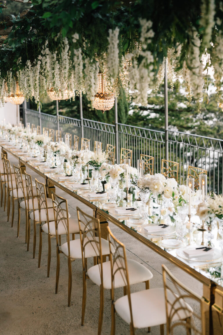 A long mirrored table under hanging wisteria and crystal chandeliers on a terrace above the sea, Amalfi Coast, Suellen Fernandes Weddings & Celebrations