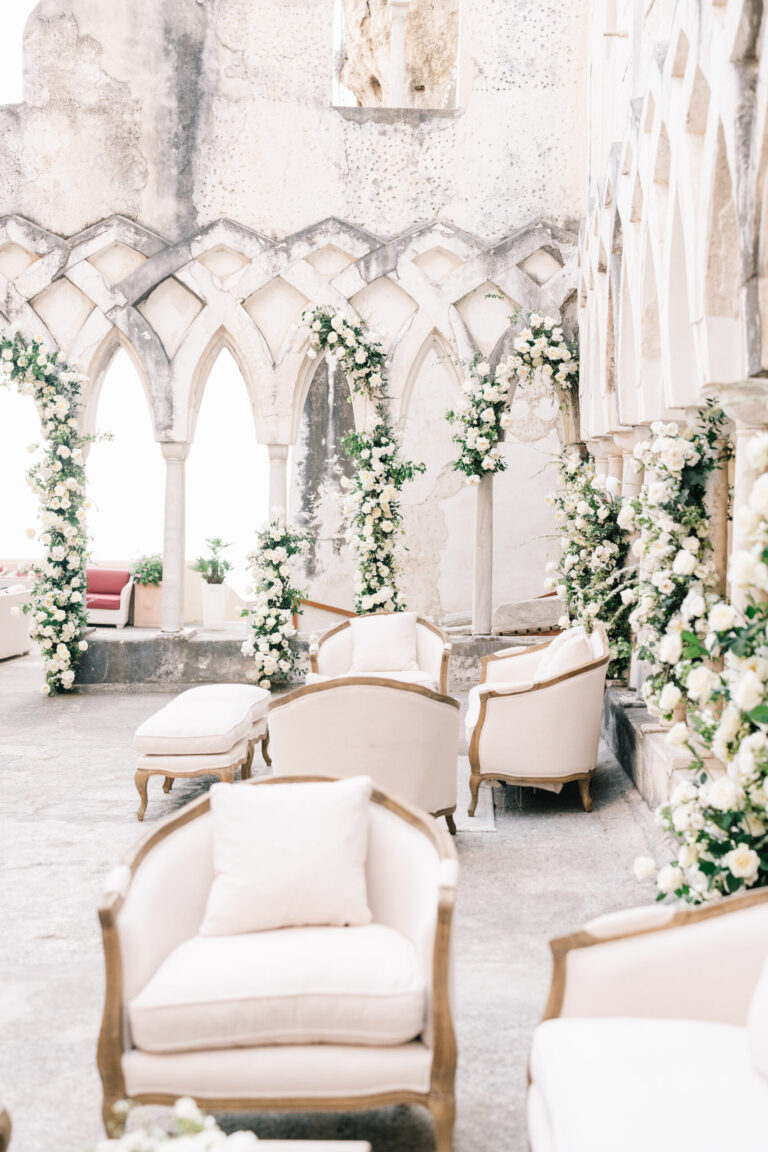 A cloister arcade on the Amalfi Coast dressed with white flowers and cream armchairs, Suellen Fernandes Weddings & Celebrations