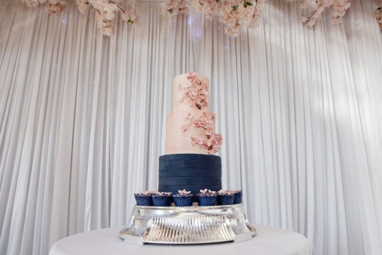 A navy and white tiered cake with pink sugar flowers and matching cupcakes, Sugar and Spiced Cakes