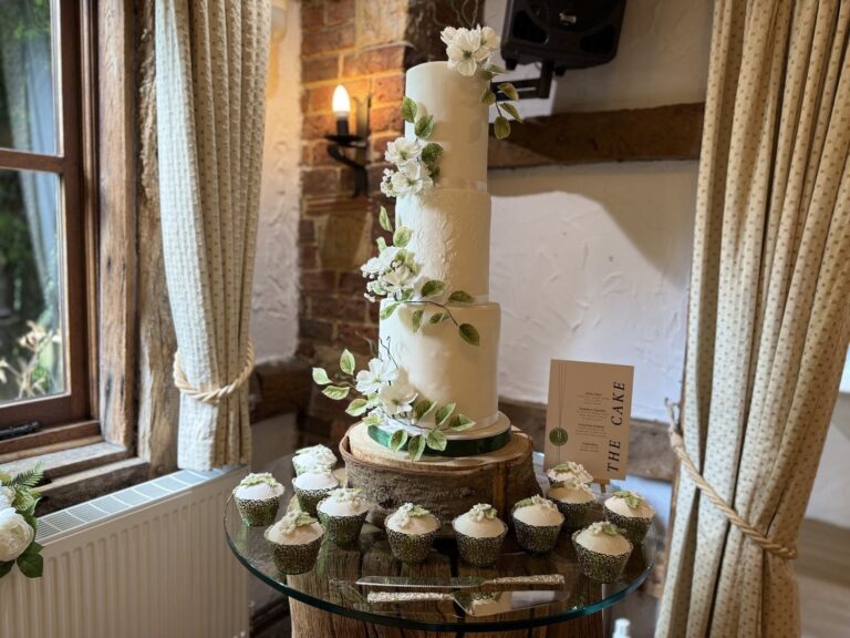 A tall cake with sugar flowers beside a dessert table of cupcakes, Sugar and Spiced Cakes