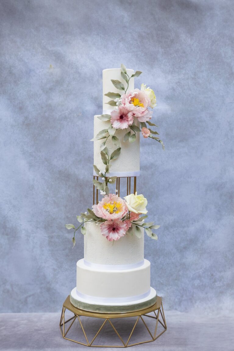 A tall tiered cake with hand-made sugar flowers on a gold stand, Sugar and Spiced Cakes