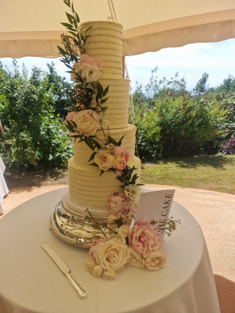 A ridged tiered cake with cream roses and foliage in a marquee, Sugar and Spiced Cakes