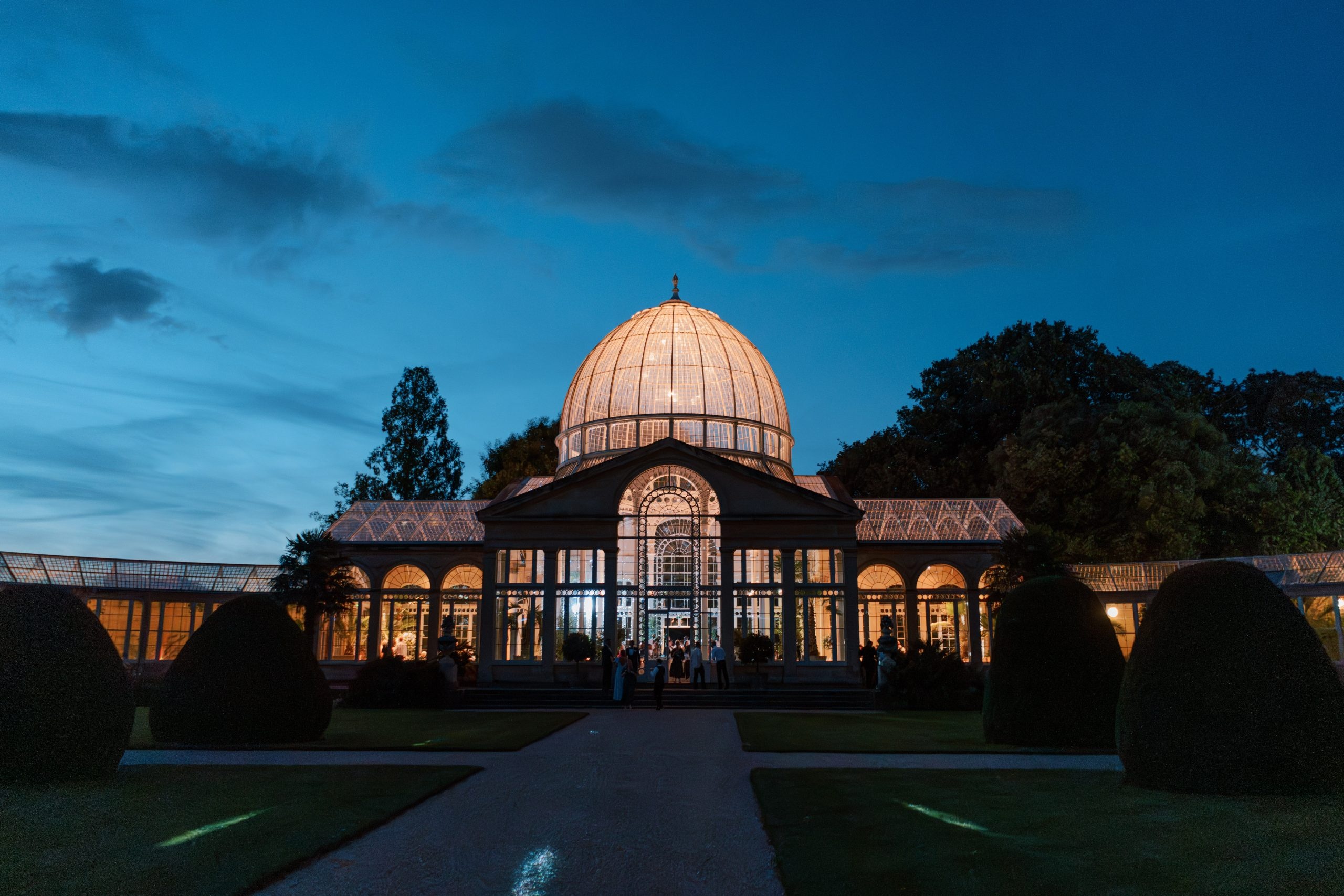The Great Conservatory illuminated gold at dusk, its domed glasshouse rising above the parterre, Syon Park