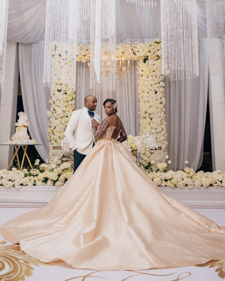 A couple in front of a white hydrangea and rose frame, beneath hanging crystal strands and a chandelier, Tai Flora Luxe