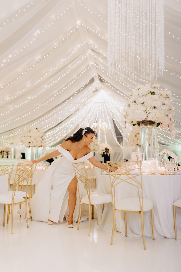 A bride seated at a floral-dressed table beneath a draped ceiling hung with fairy lights, Tai Flora Luxe