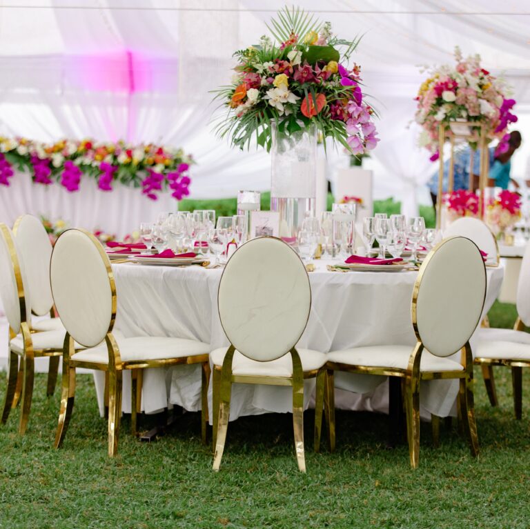 A round table with gold oval-back chairs and tall tropical floral centrepieces in pink and orange, Tai Flora Luxe