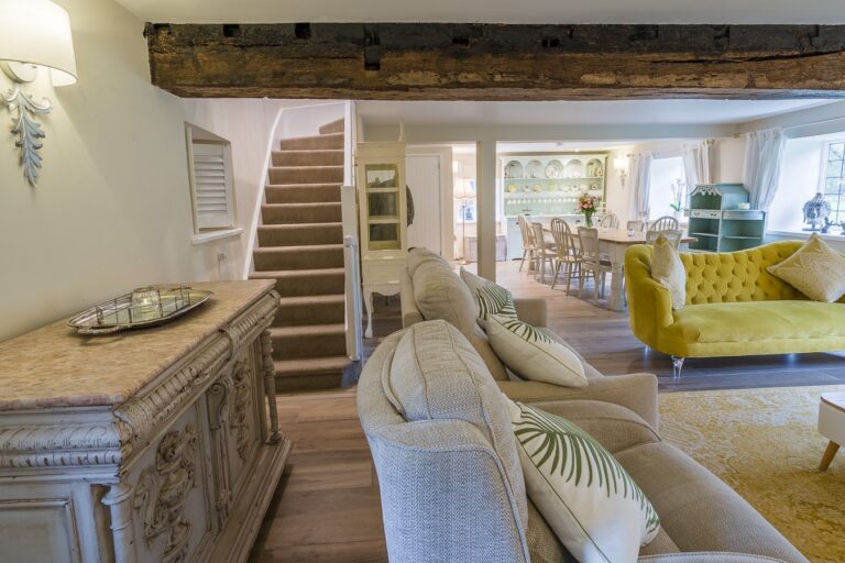 An open-plan sitting room with a beamed ceiling, stairs and a dining table beyond, Tan House Newland