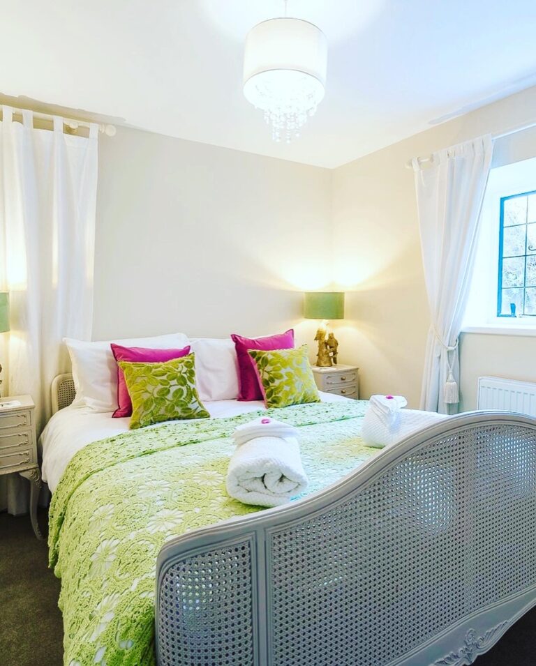 A double bedroom with a cane-headed bed, green and pink cushions and a chandelier, Tan House Newland