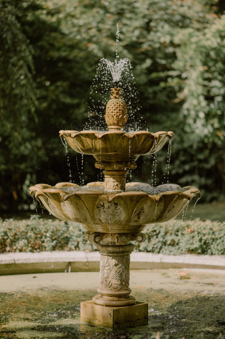 The tiered stone fountain topped with a pineapple, playing in its pool among the trees, Tan House Newland