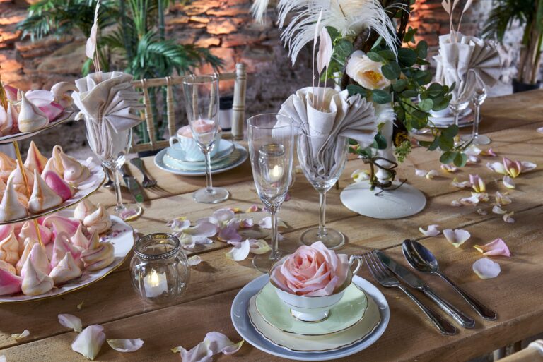 A place setting with a rose in a teacup, folded napkins and scattered petals, Tan House Newland