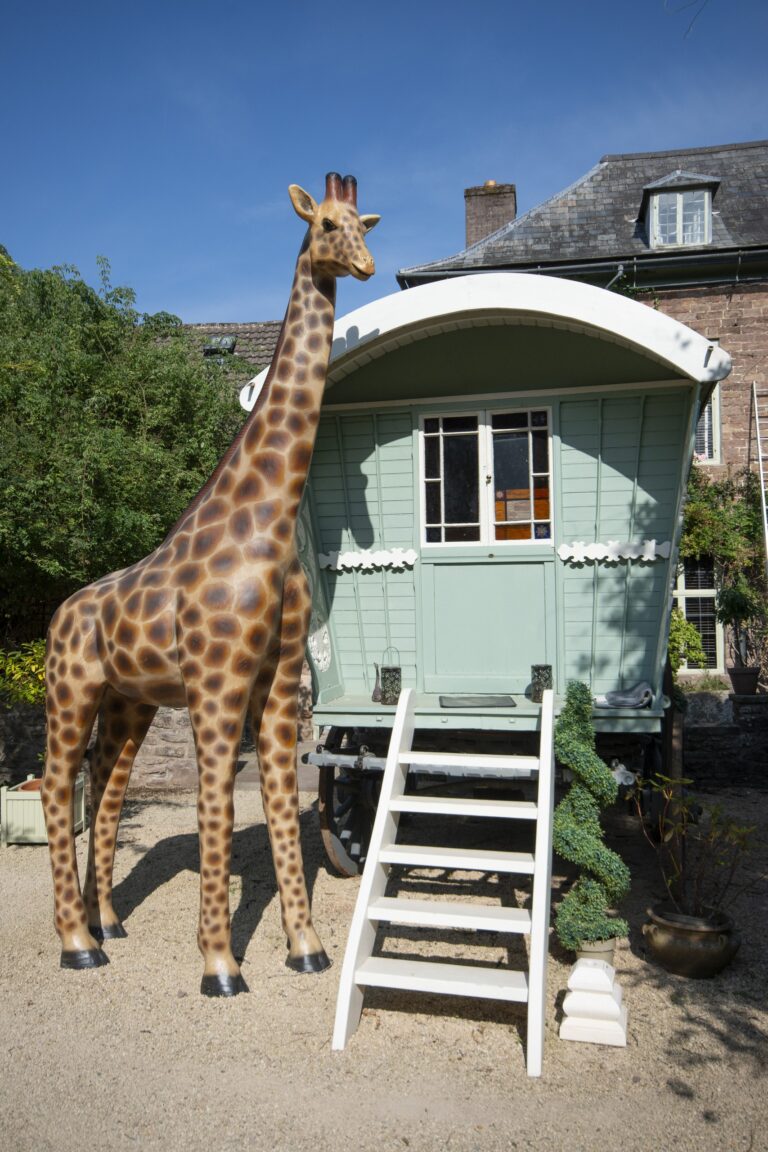 A life-size giraffe model beside a green painted wagon in front of the house, Tan House Newland
