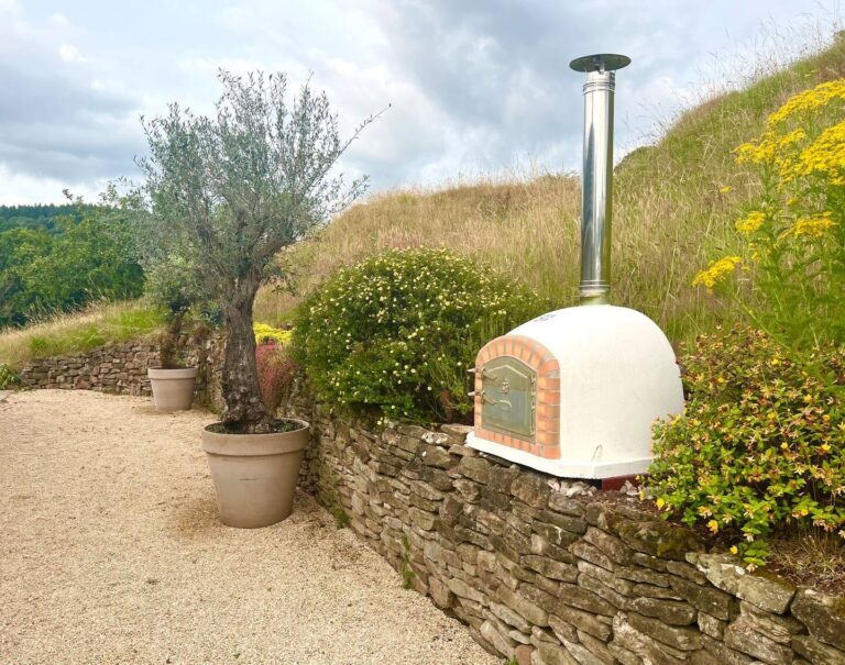 The wood-fired pizza oven on a dry-stone wall beside a potted olive tree, Tan House Newland