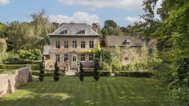 The stone house seen across its lawn, with clipped yews, a low garden wall and the old outbuildings to the right, Tan House Newland