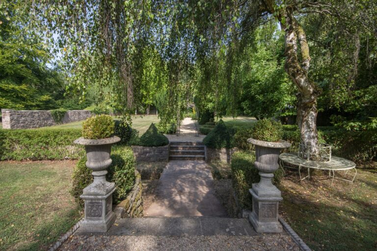 A pair of stone urns flanking steps down to a garden path under weeping willows, Tan House Newland
