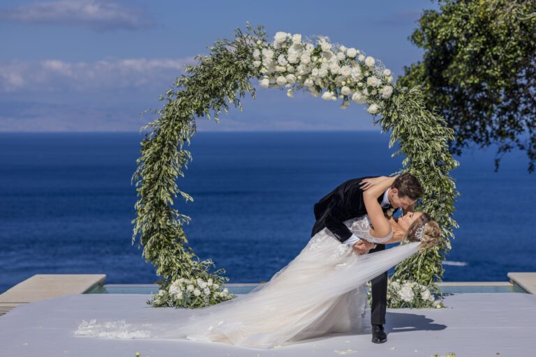 The couple kiss under a circular olive and white rose arch above the Ionian Sea, Taormina Weddings