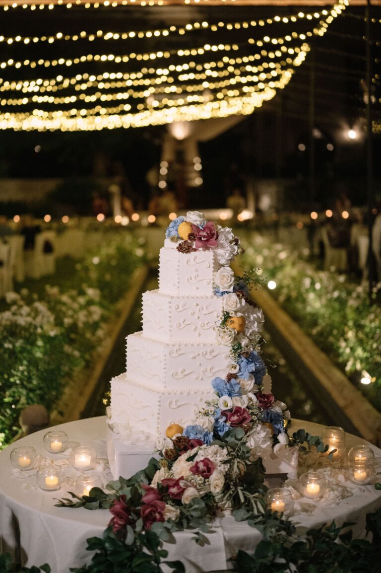 A four-tier iced cake with hydrangea, orchids and lemons under fairy lights, Taormina Weddings