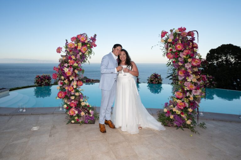 Two towers of pink and red flowers either side of an infinity pool at dusk, Taormina Weddings