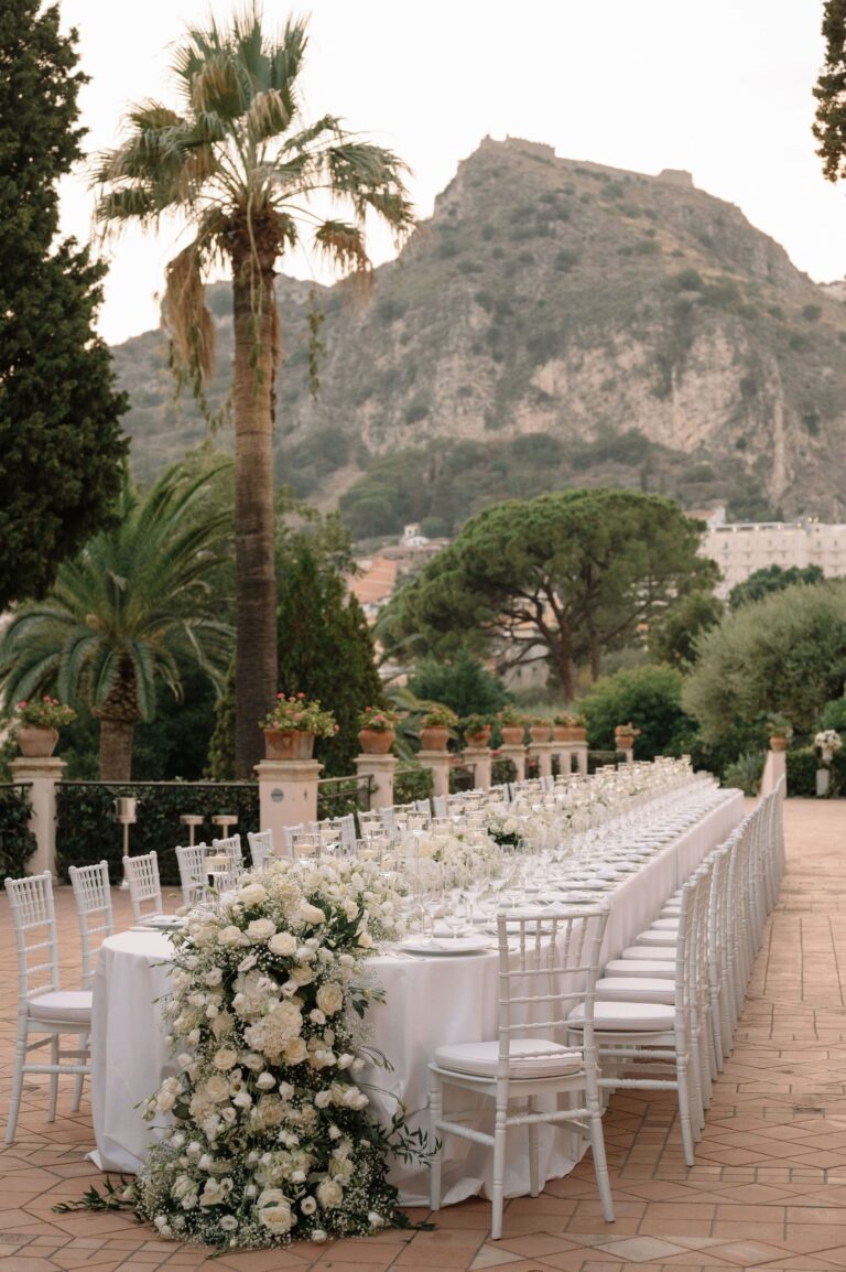 A long white table on a terrace, palms and the rock above Taormina behind, Taormina Weddings