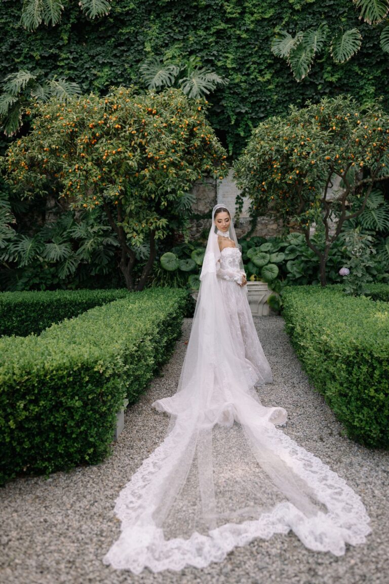 The bride in a walled garden between box hedges, her long veil on the gravel, Taormina Weddings