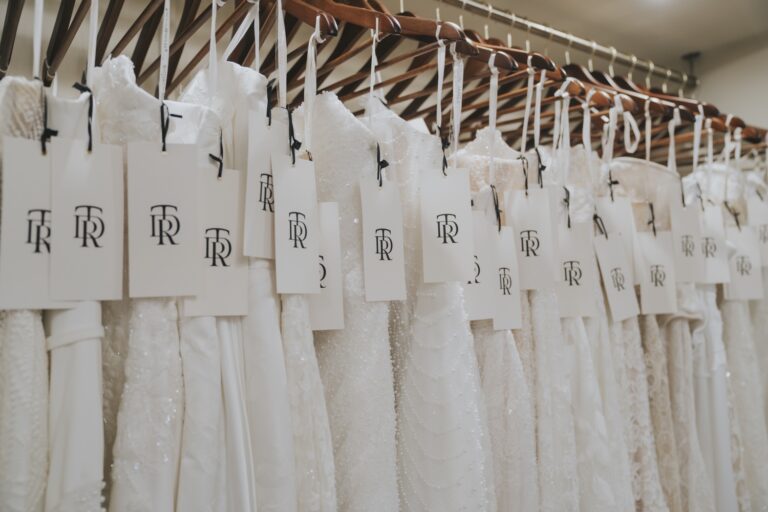 A rail of white wedding dresses hung with TDR luggage tags, TDR Bridal