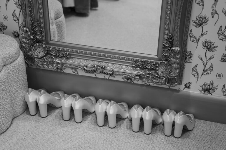 A row of white bridal shoes beneath a gilt mirror, in black and white, TDR Bridal
