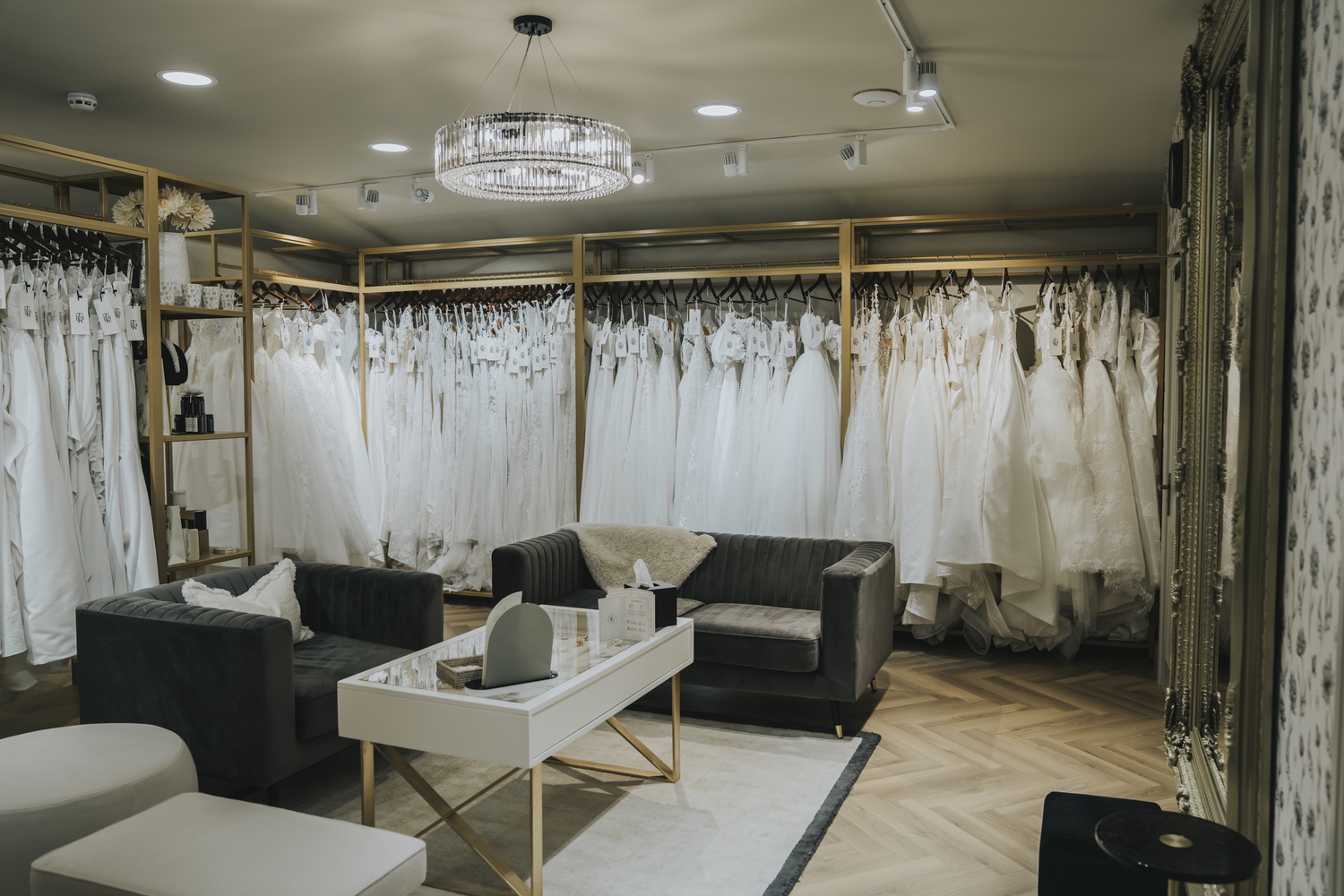 A private bridal suite with dark velvet sofas, a white coffee table and a wall of wedding dresses, TDR Bridal