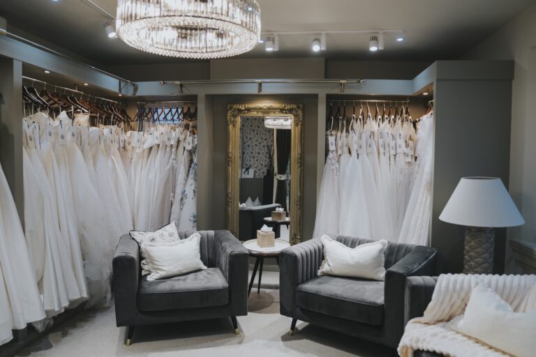 The Promise suite with two grey armchairs, a lamp and gowns hanging either side of a mirror, TDR Bridal