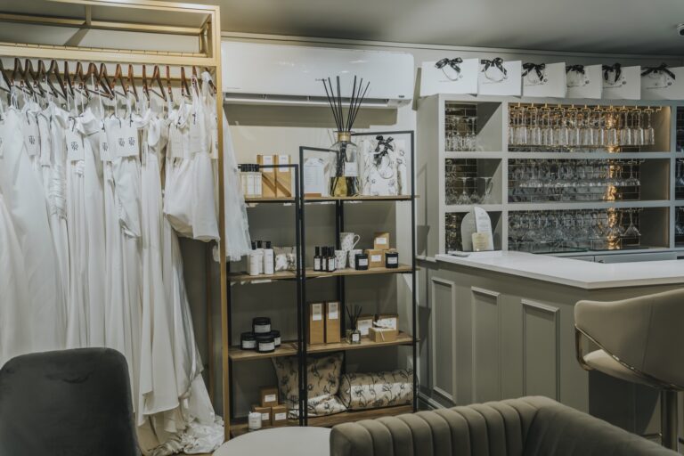 Wedding dresses beside a shelf of scented candles, glasses and gift bags in the Beloved suite, TDR Bridal