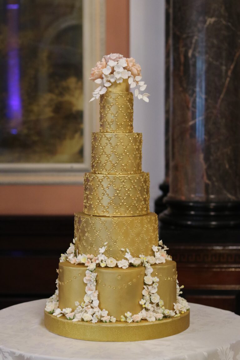 A five tier gold wedding cake with quilted texture and white sugar blossom, Tees Bakery