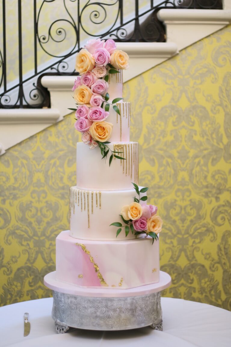 A tiered cake with pink marbling, drip detail and sugar roses on a metal stand, Tees Bakery