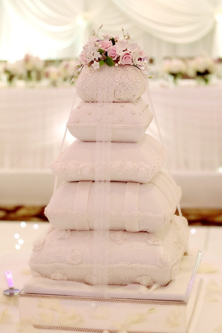 A stack of sugar pillows in pale pink forming a wedding cake topped with flowers, Tees Bakery